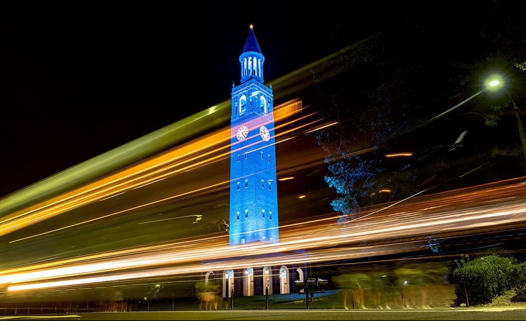Car drive by the Bell Tower, which is lit in Carolina Blue.